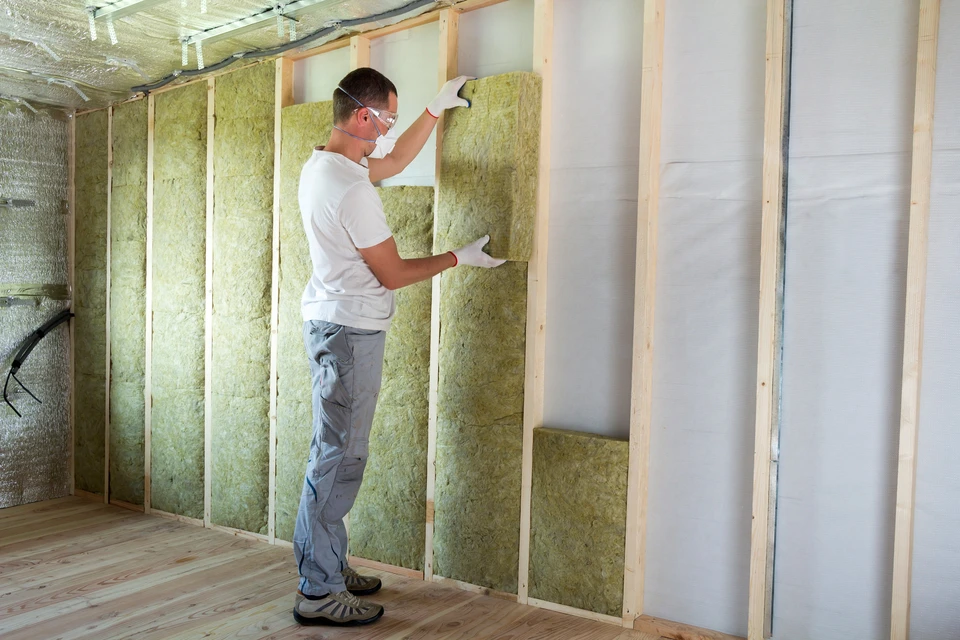 Ouvrier en équipement de protection individuelle installant l'isolation thermique dans une construction résidentielle
