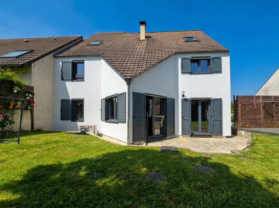 Maison individuelle à deux étages, façade blanche avec volets battants anthracite, toiture en tuiles brunes avec lucarnes à tabatière