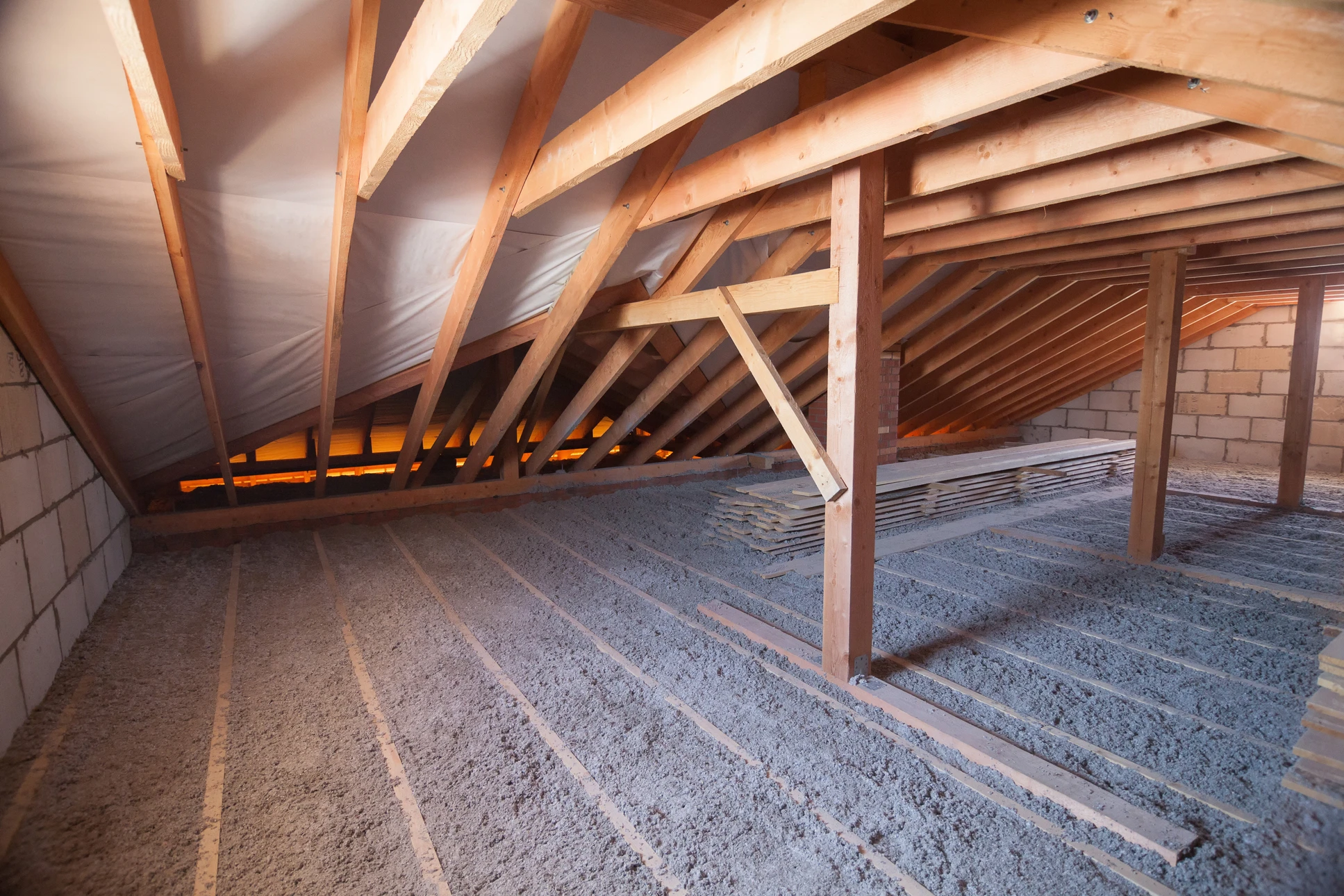 Ouvrier installant de l'isolation thermique entre les solives d'un plafond dans un grenier