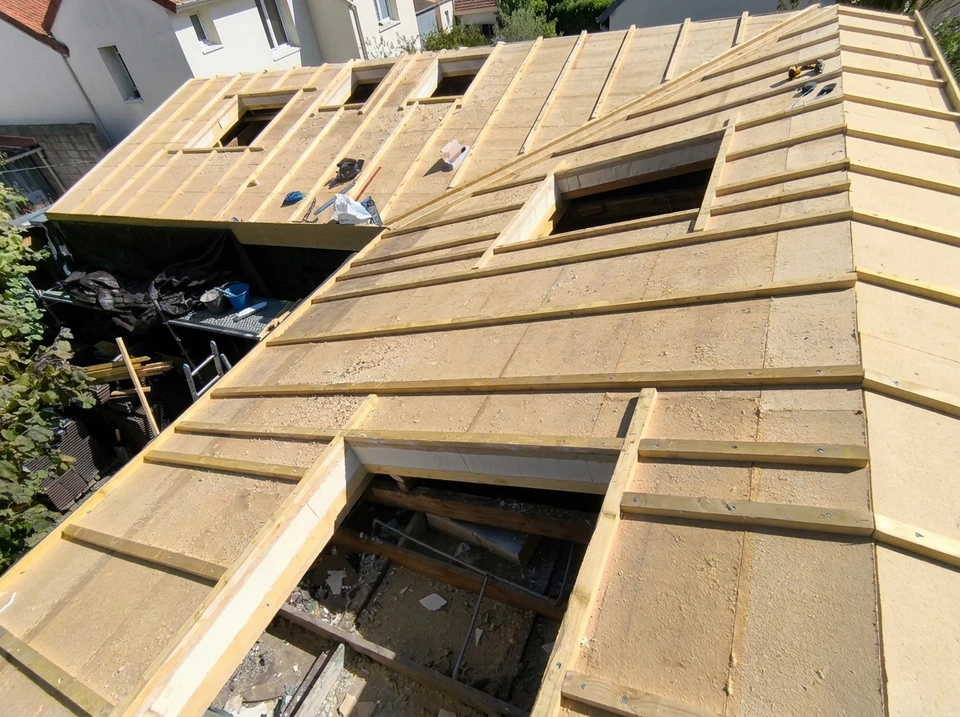 Ouvrier installant des tuiles sur toiture en cours de rénovation, laine de verre isolante visible entre chevrons